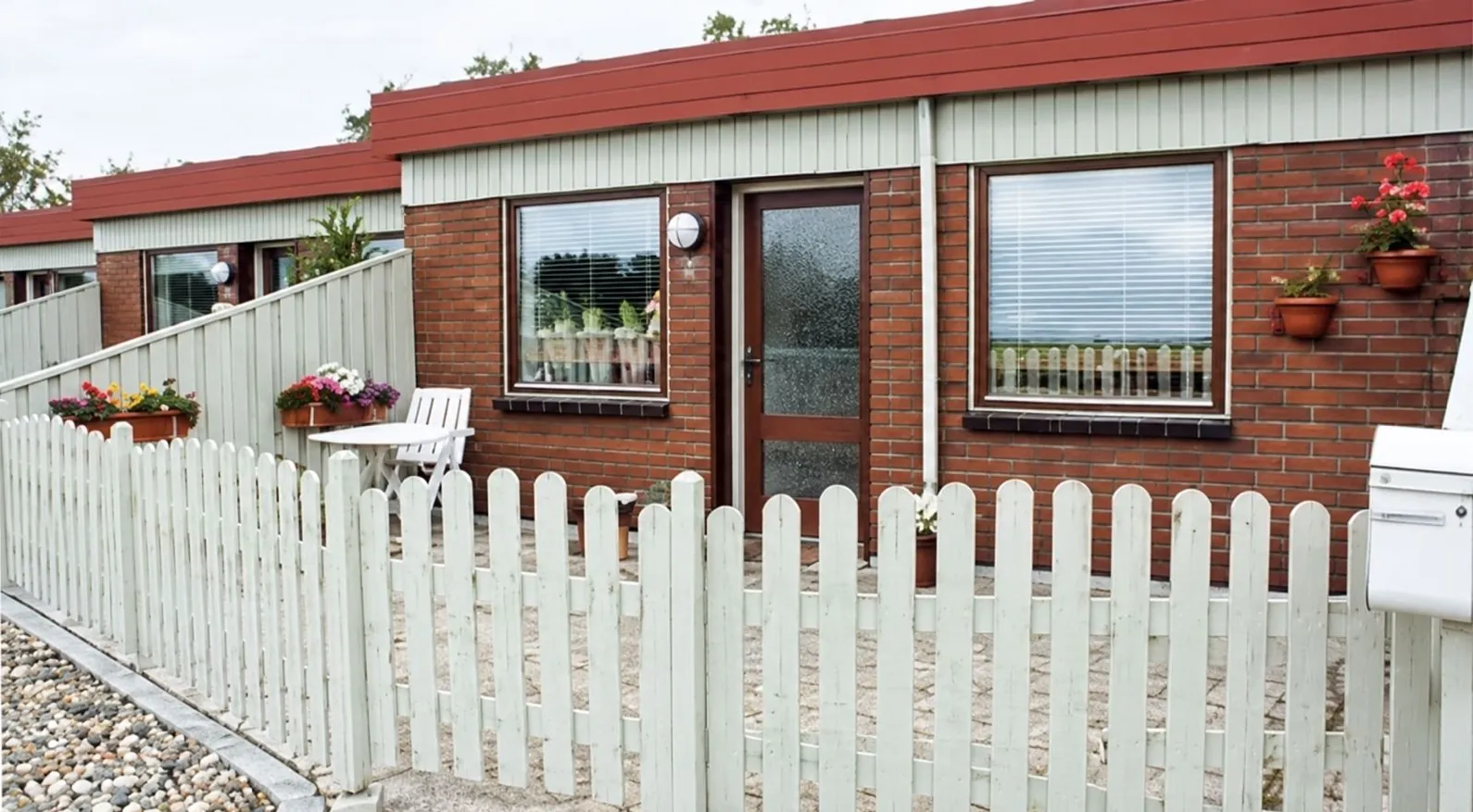 Rækkehus i Stengården: røde mursten, hvidt stakit og blomster i forhaven